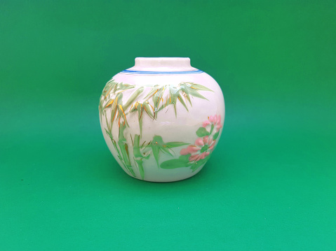 A small ceramic urn for indoor decoration with a white base color combined with relief ornaments on the outside, isolated on a green background