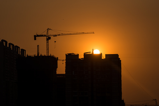 Sun sets behind a tall skyscraper under construction in the suburb of Kandivali in Mumbai.