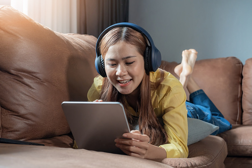 Asian girl listening to music with her digital tablet on sofa, leisure concept.