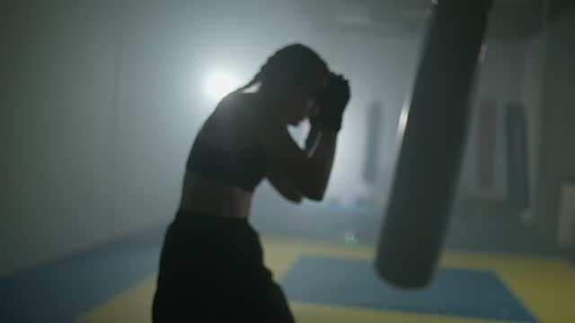 Blurred view of woman fighter trains his punches and defense in the boxing gym, contour lighting, 4k slow motion.