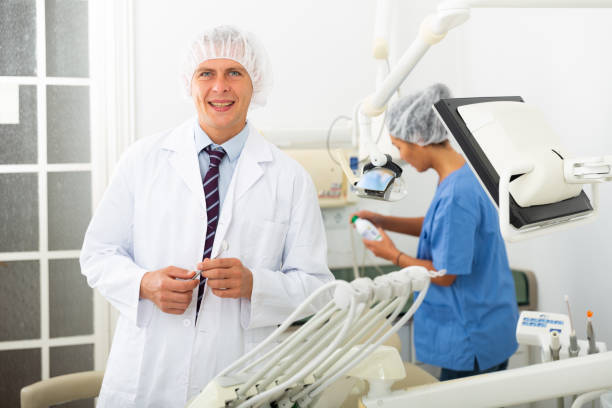 Portrait of a qualified smiling man dentist standing at his workplace in the clinic office