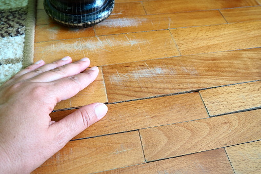 Scratched old parquet flooring needs maintenance. The parquet is damaged by scratches from prolonged use. Master's hands show damage to the floor. The leg of an antique wooden bed.