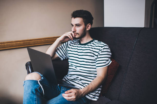 istock Young man propping chin while sitting on sofa with laptop 1446263674