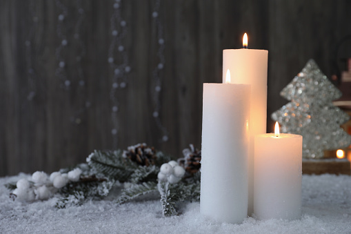 Burning candles and Christmas decor on artificial snow. Space for text