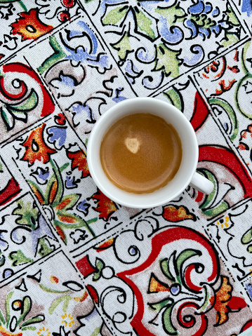Direct view from the top on a coffee cup placed on the table. The table is covered in Sicilian traditional tiles. Espresso in a cup is hot and aromatic.