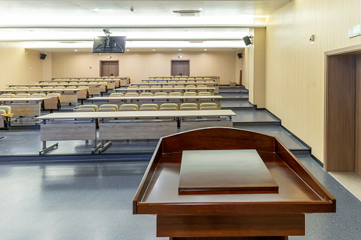 A seminar / meeting room. There are a blank screen, two podiums with microphones, a projector, tables and chairs in the room. 