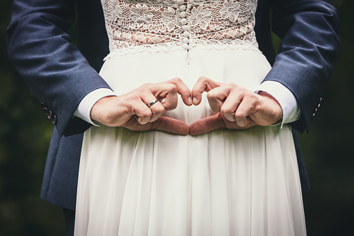 a bride and groom with wedding rings form a heart with their hands on the woman's back