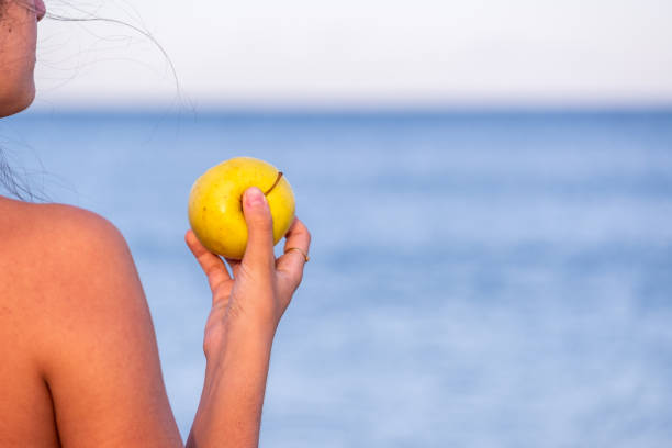 Young woman eating a yellow apple on a beach at sunset