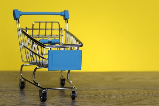 Mini shopping trolley on yellow background with copy space. Shopping and consumer concept.