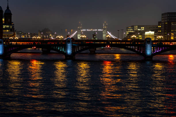 Majestic night image of London's iconic Tower Bridge, brightly lit against the dark sky. The golden and blue lights reflect its elegance over the calm waters of the River Thames. Perfect to illustrate the architectural beauty and vibrant nightlife of London