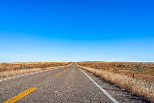 Road trip point of view near Wichita, Kansas rural countryside with wide angle view of clear blue sky and empty street paved way by dry farm fields in autumn fall season stock photo