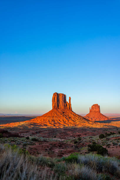 Monument Valley famous buttes vertical view at colorful red sunset in Arizona with orange rocks formations and blue sky with east and west mittens shapes stock photo