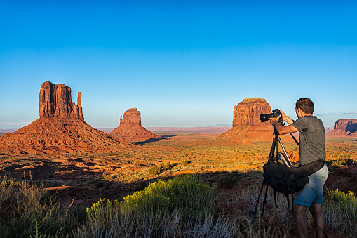 Famous buttes and horizon view in Monument Valley at sunset light in Arizona Utah border with orange rocks and man photographer taking picture from tripod
