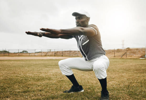 istock Baseball player, stretching and black man on sports field doing warm up exercise, workout practice for match. African male athlete outdoor with tshirt and cap for health, wellness and energy on pitch 1446299239