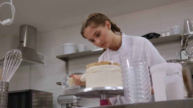 A chef rotating a cake on a turntable and squeezing cream from a pastry bag.
