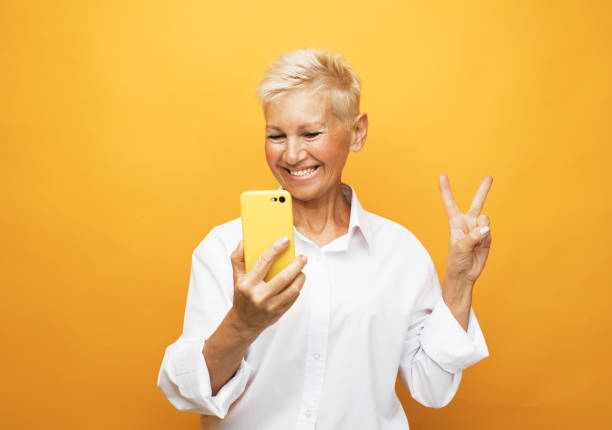 Image of cheerful mature old woman standing isolated over yellow background wall talking by mobile phone. stock photo