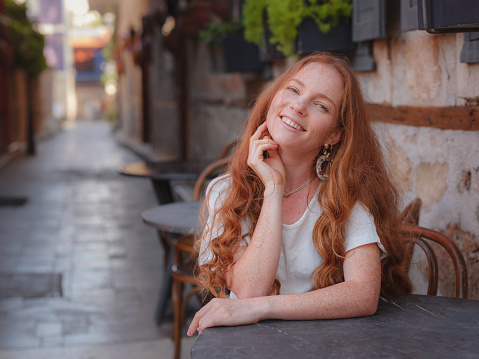 Happy woman tourist on background of blooming street. female traveler discover interesting places and popular attractions and sitting at table on terrace in old city Kalechi of Antalya, Turkey.