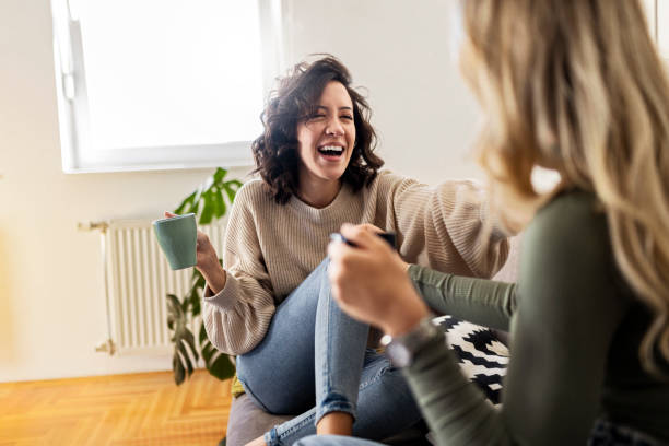 Two young women having coffee and chatting having great time Two young women having coffee and chatting while sitting in a living room female-friendship stock pictures, royalty-free photos & images