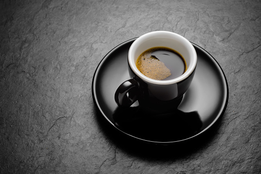 Espresso coffee in small porcelain mug with on the black slate.