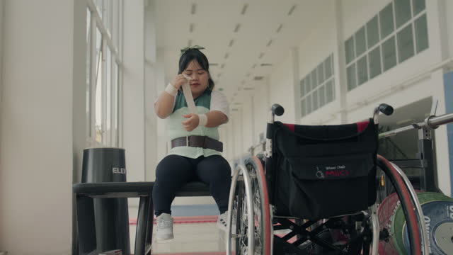 Young woman with disability in wheelchair preparing to train in gym.