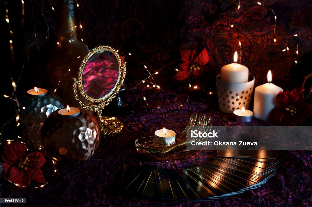 Blurred Tarot cards on table near burning candles. Tarot reader or Fortune teller reading on Christmas decoration Defocused mystic ritual with tarot cards,  and candles. Christmas concept, black magic or fortune telling rite with occult and esoteric symbols. Magician Stock Photo