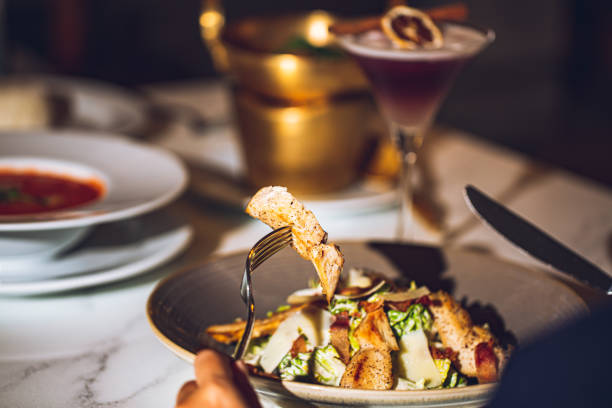 Woman's hands sitting at restaurant table holding fork and ready to eat caesar salad