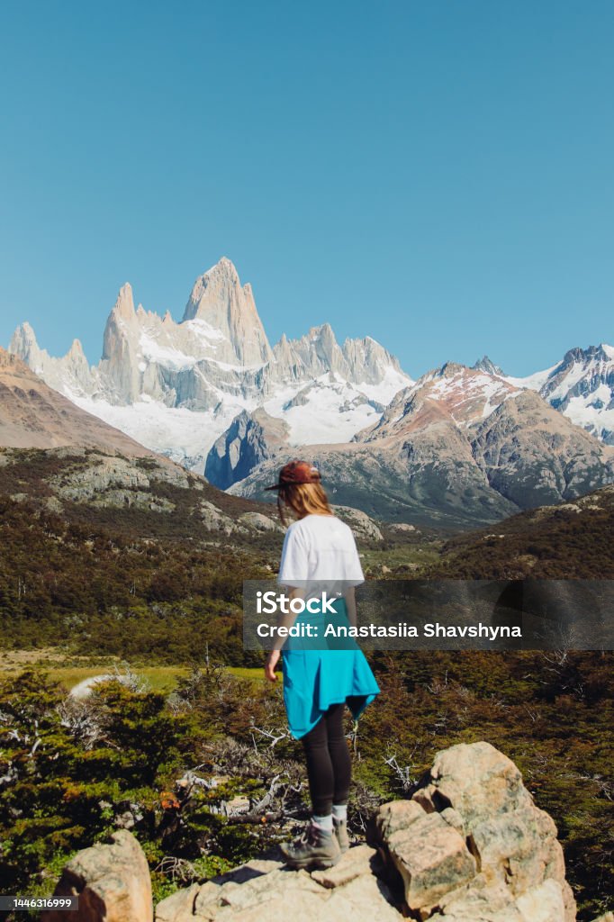 Rear view of a woman contemplating a view of Fitz Roy mountains in Patagonia during the hiking trip Female explorer in cap looking at majestic mountain range in the beautiful vast valley in El Chalten, Argentina Adult Stock Photo