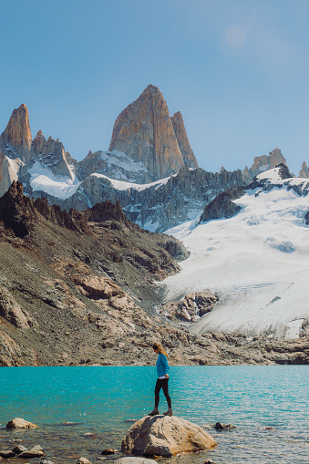 Female explorer hiking to the turqouise glacial lagoon with view of majestic mountain range in El Chalten, Argentina