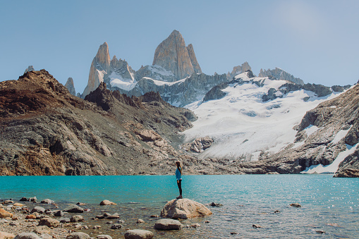 Female explorer hiking to the turqouise glacial lagoon with view of majestic mountain range in El Chalten, Argentina