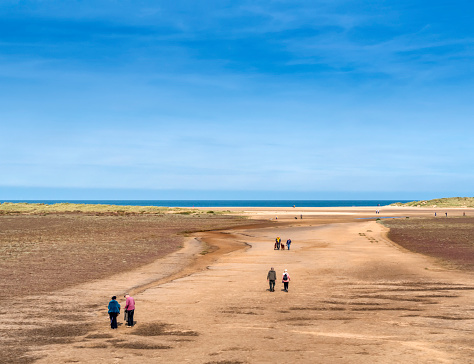People and dogs walking on the wide sands in Holkham bay on the north coast of Norfolk, Eastern England. The golden sands extend for miles and are popular with dog walkers, horse riders and, of course, holidaymakers.