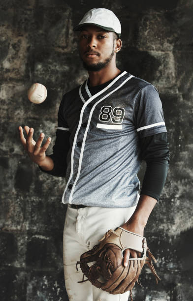 istock Baseball, sports and uniform with a man athlete on a dark background wearing a mitt while holding a ball. Portrait, sport and confident with a male baseball player standing against a dugout wall 1446322013