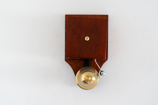 Close up view of wooden vintage doorbell ringing, hanging on white copy space wall in building. Design element in classic style at modern apartment
