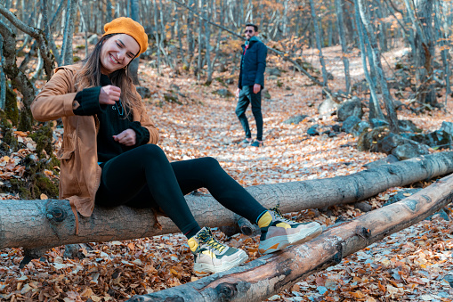 in the foreground the woman is happy, in the background the man looking from afar is sad. relationship problem and contradiction. This moment between the fallen leaves in the forest was shot with a full frame camera.