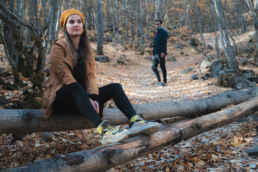 Separation image of couple in forest in autumn season. The man turns his back and leaves, the woman sits on the timber and is sad. This moment between the fallen leaves in the forest was shot with a full frame camera.