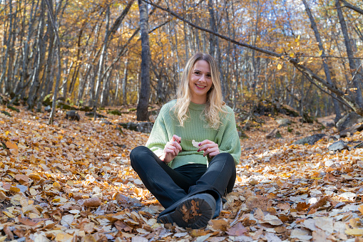 Beautiful woman sitting and resting in the forest in autumn season.. She spends a quiet time among the yellowed leaves. Shot with a full frame camera.