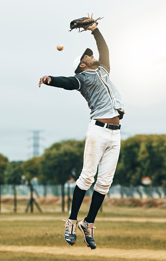 Baseball, sport and person fielder jump on an outdoor sports field during sport game or match. Fitness, training motivation and cardio workout of an athlete man with focus ready to catch a fast ball