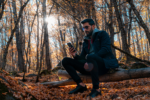 In the autumn season, the young man was photographed in the forest. He spends a quiet time among the yellowed leaves. Shot with a full frame camera.