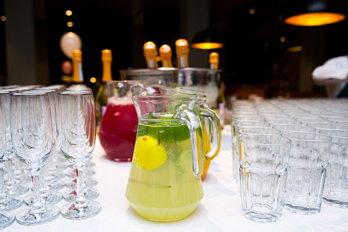 Soft drinks lemonades in large glass jugs on the table surrounded with empty glasses