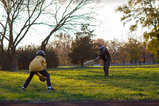 Father plays baseball together with his son at park.