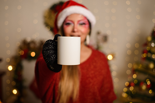 Young woman with Christmas fantasy makeup holding white mug. Selective focus on the mug. Christmas background.