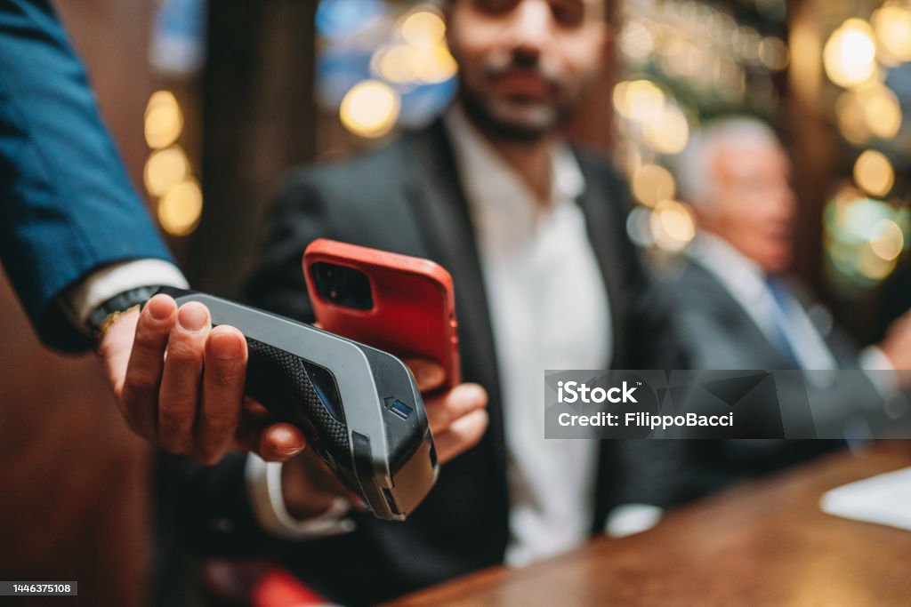 A man is paying the bill at the restaurant using his smart phone A man is paying the bill at the restaurant using his smart phone. High-end luxury restaurant. Paying Stock Photo