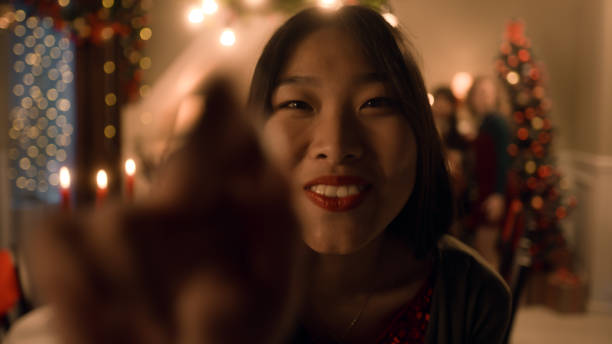 Asian woman sets timer on camera or phone. Happy multi cultural family takes group photo. They celebrating Christmas or New Year. Table with dishes and candles. Family Christmas dinner. Camera view.