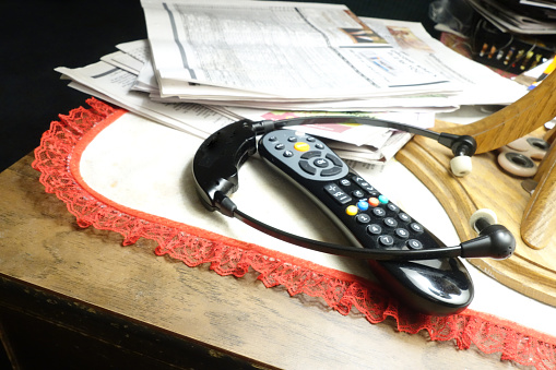 Electronic Ear Phones and Television Remote Control on Untidy Table with Stack of Old Newspapers