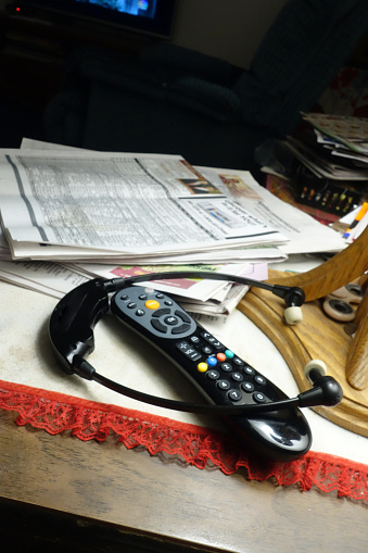 Vertical Potograph of Electronic Ear Phones  and Television Remote Control on untidy Table amid Stack of old Newspapers