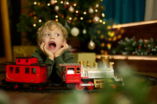 istock Happy curly-haired boy is playing with a magic toy train at the Christmas tree. 1446392699