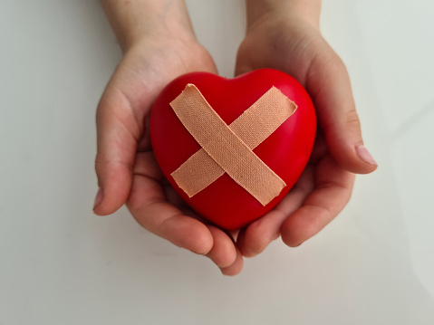 Child holds broken heart sealed with band-aid. Heart and cardiovascular diseases and treatment