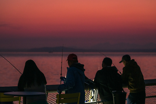 Seattle, USA - Oct 9th, 2022: A vivid sunset on Elliott bay off pier 62 as people fish in the unusually warm weather.