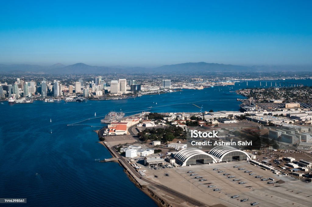 Aerial view of North Island Naval Air Base on Coronado and downtown San Diego California while flying over the bay with boats on the water and mountains in the background during daylight San Diego California is the southern most city in California right by the Mexico border. It is often referred to as America's Finest City due to it's pleasant yearly weather Military Base Stock Photo