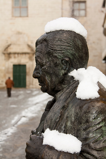 Lugo, Spain- January 8, 2010: Lugo city street view covered with snow . Writer, author Anxel Fole bronze statue in the foreground.  Lugo city, Galicia, Spain.