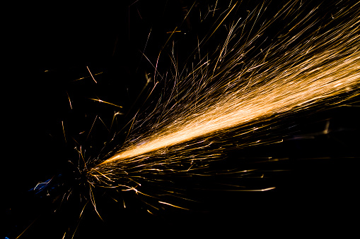 Close-up of three sparklers shaped as 'NUMBER 100' emitting sparks while burning against black background.